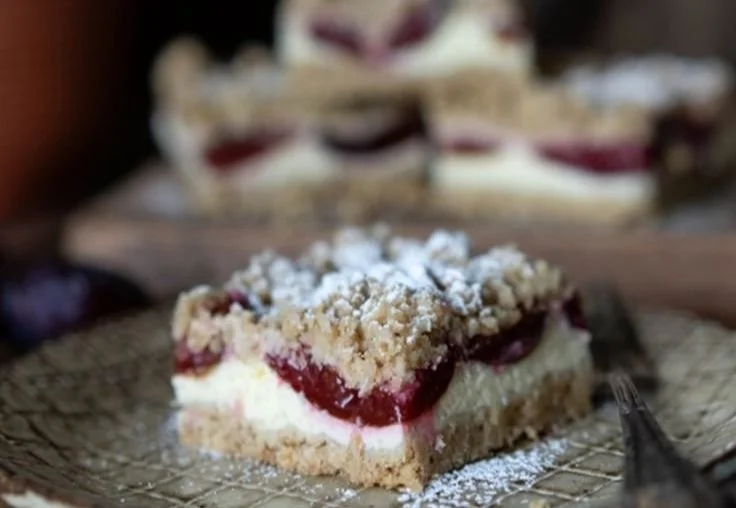 Pflaumen-Cheesecake auf einem Teller mit frischen Pflaumen und Sahne